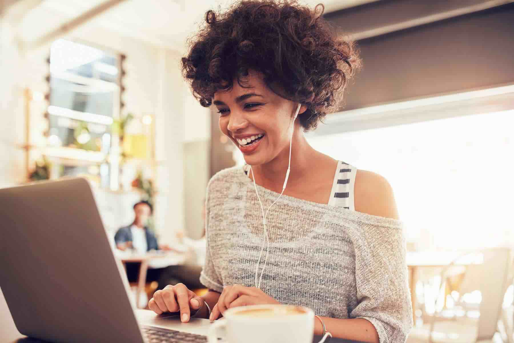 Image of happy woman using laptop while sitting at cafe. Young african american woman sitting in a coffee shop and working on laptop.