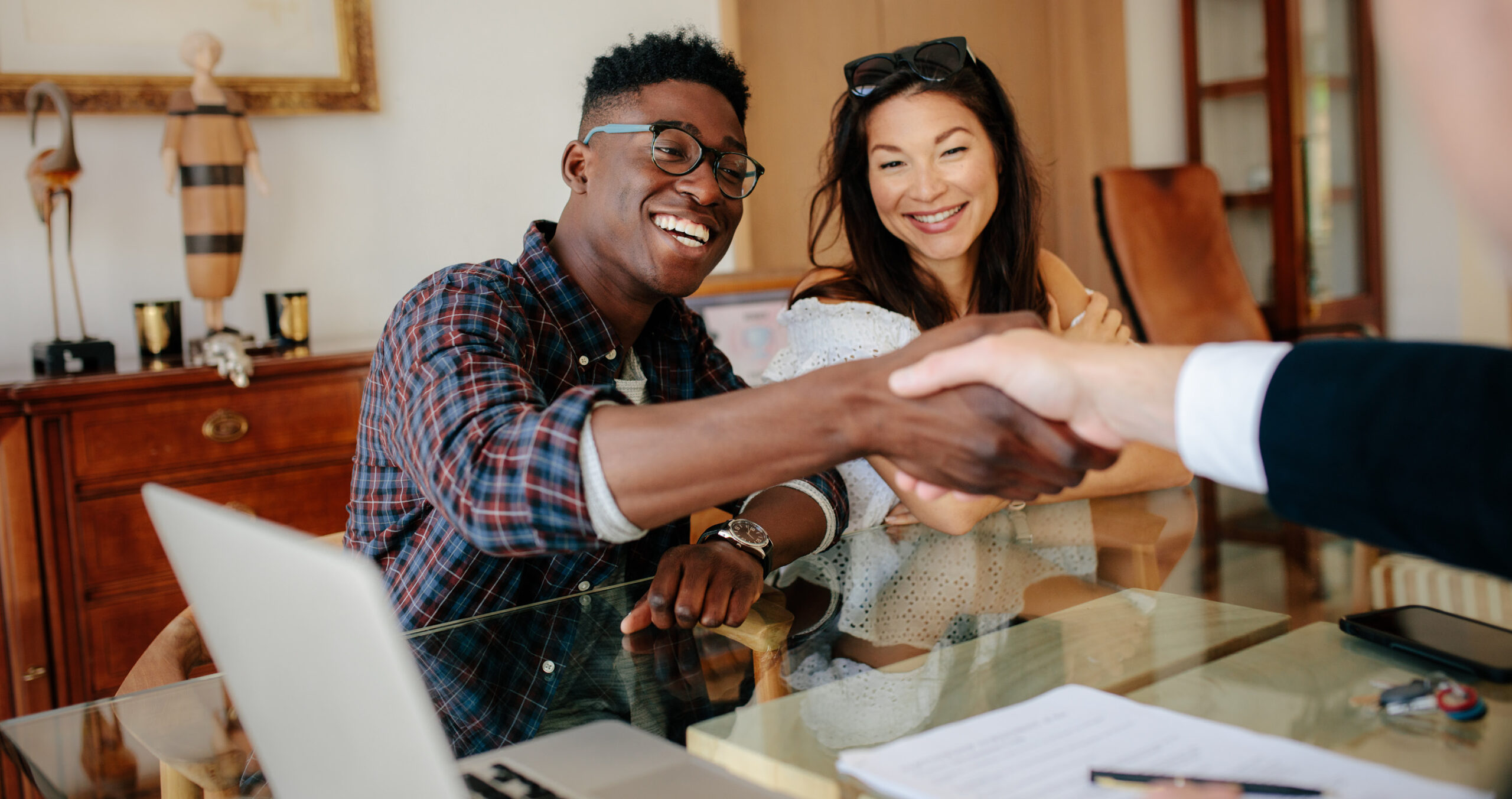 Diverse couple shaking hands with mortgage lender during loan application process in office setting