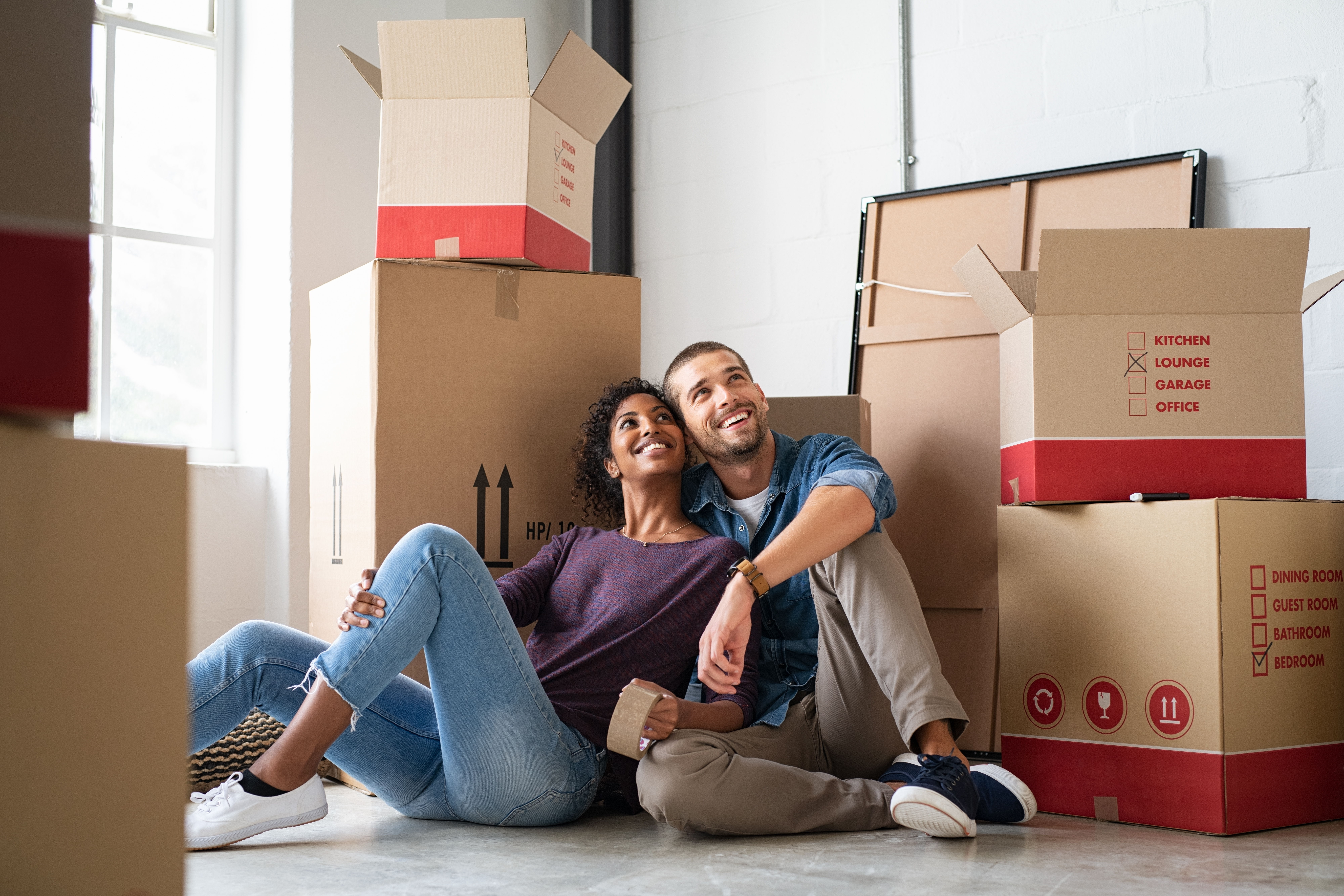 Young couple resting after moving into a new home and daydreaming. Multiethnic contemplative couple sitting on floor and thinking about their future while looking up.