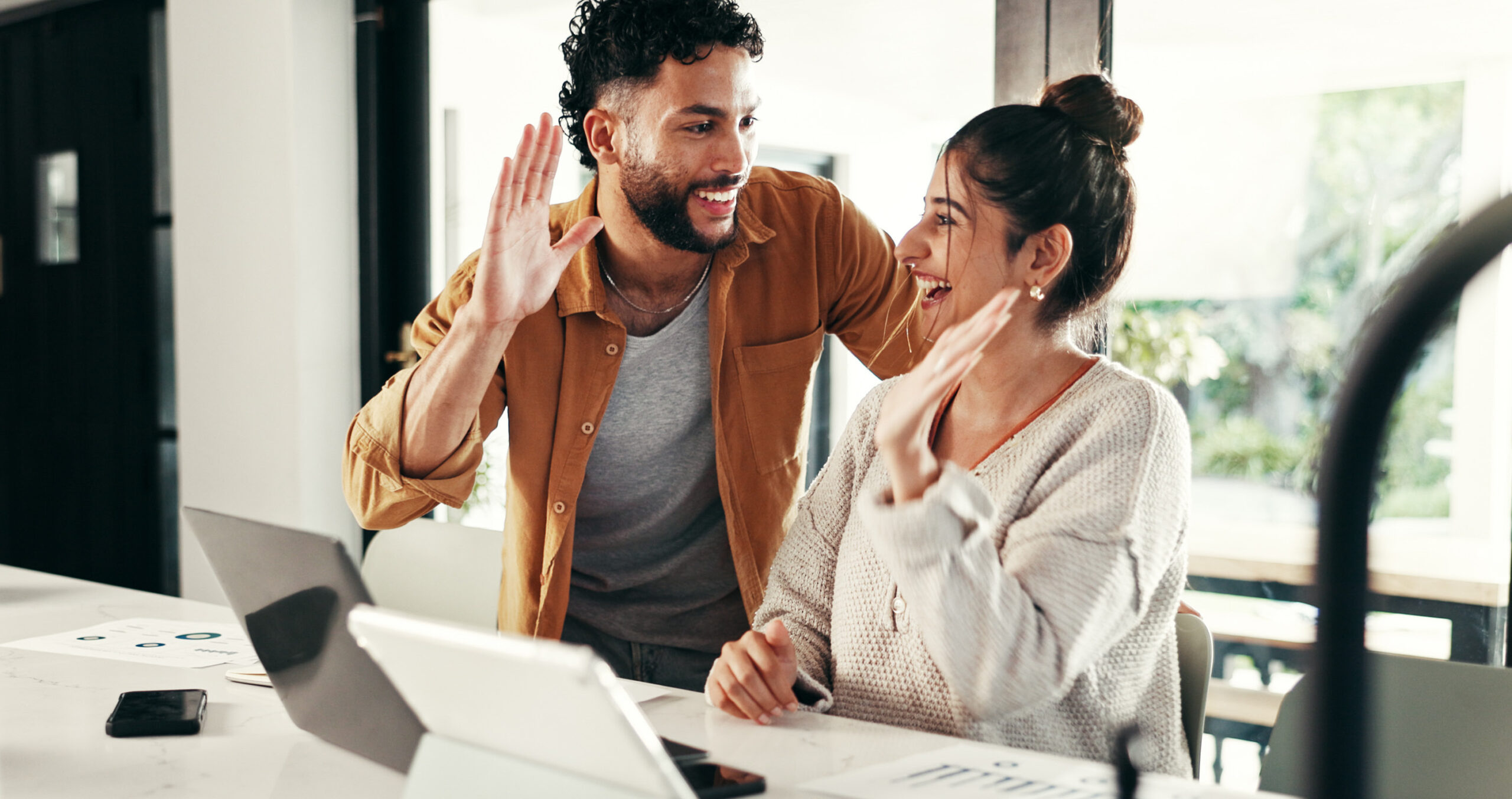 Couple celebrating meeting financial goal of building equity in their home by high-fiving at table over computer.