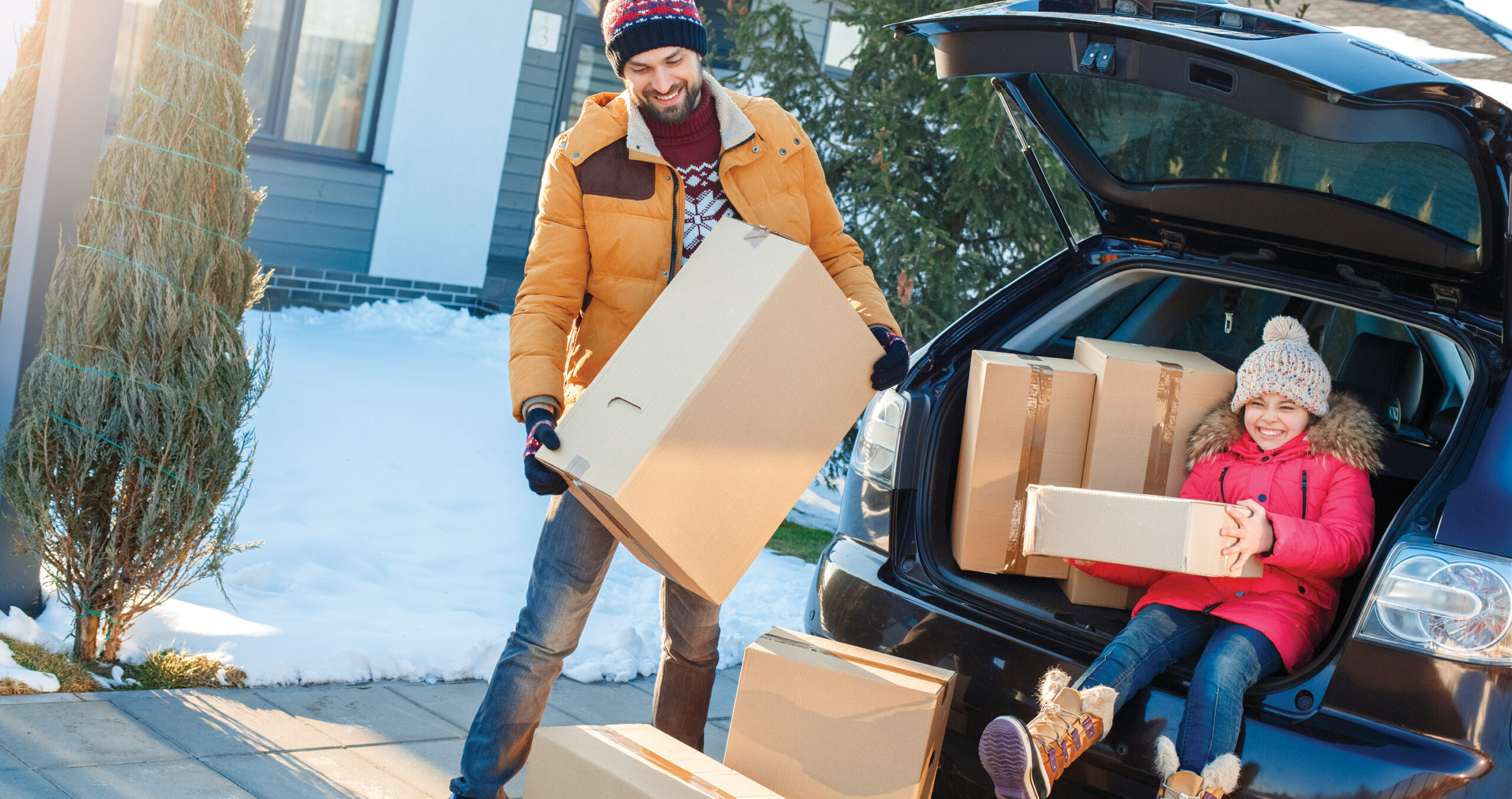 Dad and daughter moving boxes out of car into new home during winter holiday.